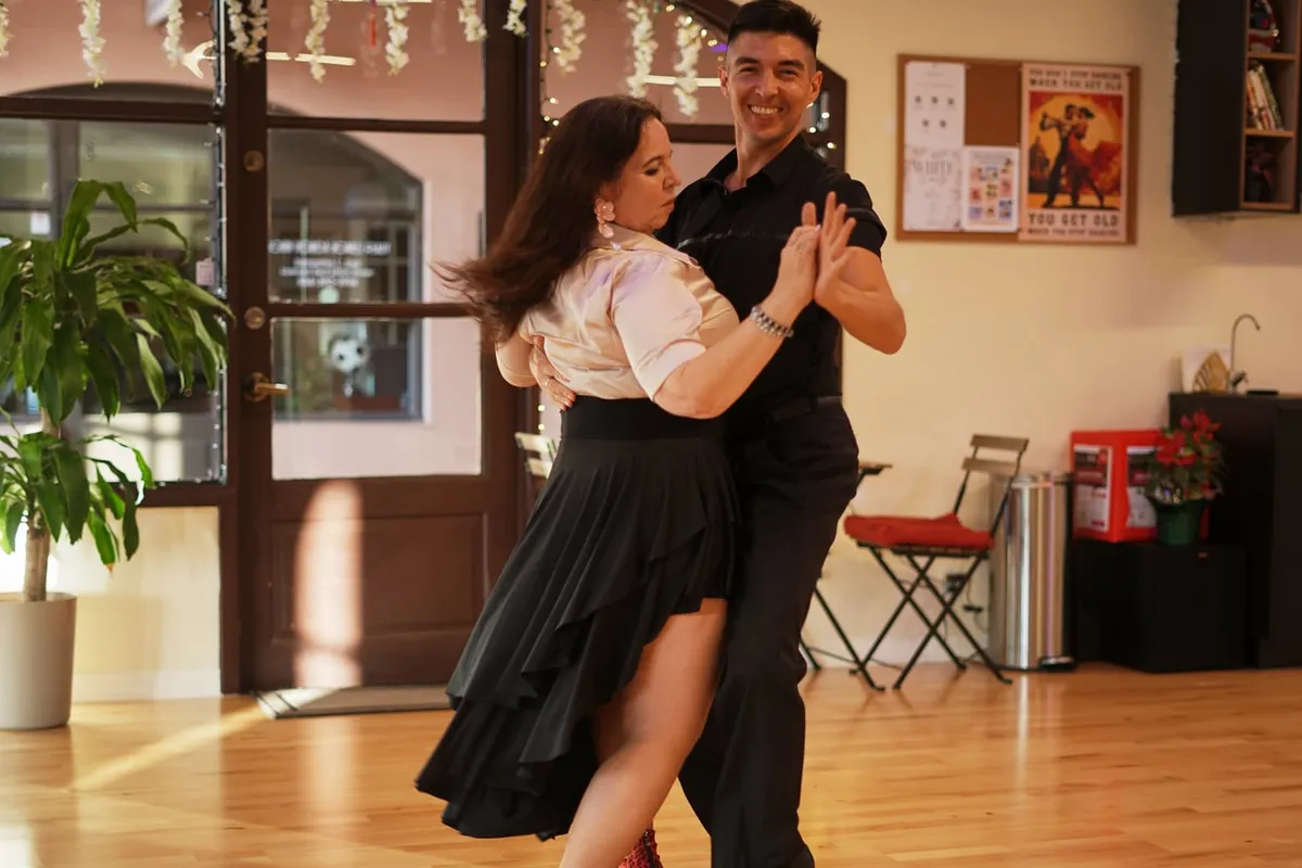 A couple in a close argentine tango embrace on the studio floor.